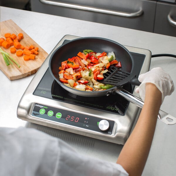 A woman using a Vollrath Mirage Pro countertop induction cooker to cook vegetables on a professional kitchen counter.
