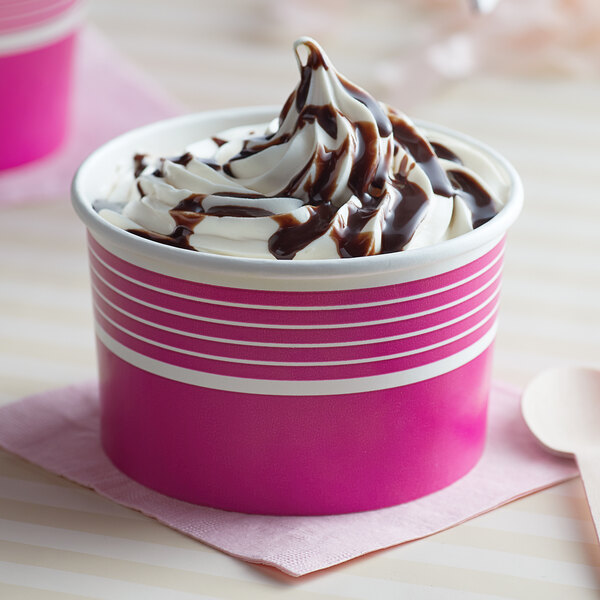 A pink paper Choice frozen yogurt cup filled with chocolate ice cream and chocolate syrup.