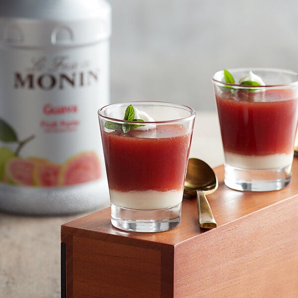 Two glasses of Monin guava fruit juice with mint leaves on a wooden tray.