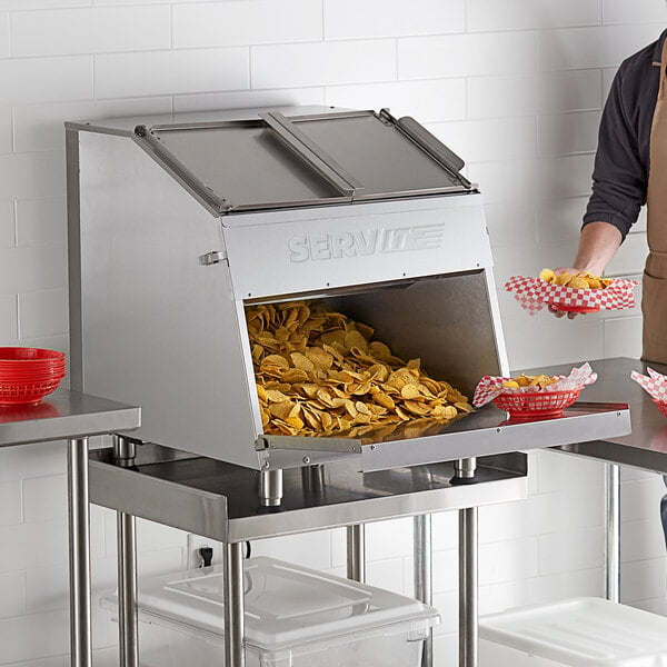 A ServIt nacho chip warmer with a large container full of chips on a counter.
