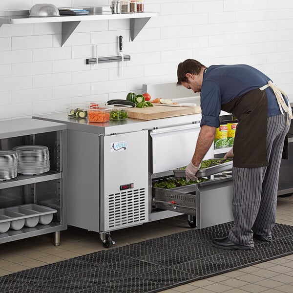 A man in a professional kitchen using an Avantco undercounter refrigerator to put food in a dish.