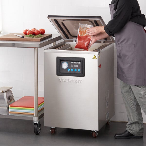 A person using a VacPak-It floor model chamber vacuum packaging machine to vacuum food into a rectangular bag.