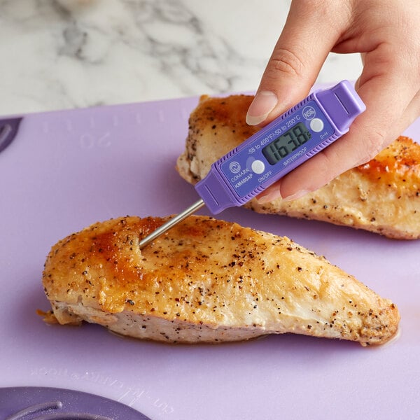 A person holding a Comark purple digital pocket probe thermometer to a chicken breast.