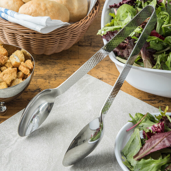A bowl of salad with lettuce leaves and Carlisle Terra stainless steel tongs on a table.