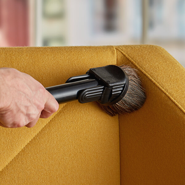 A hand using a Lavex dusting brush to clean a couch.