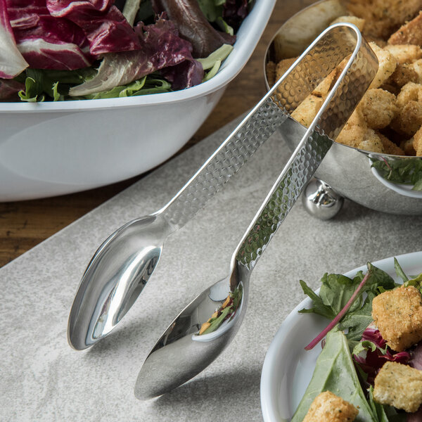 A pair of Carlisle stainless steel tongs in a bowl of salad.