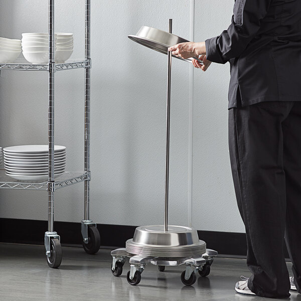 A person in a black uniform using an American Metalcraft aluminum plate cover cart to transport dishes.