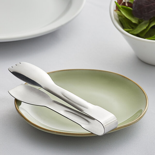 A plate with a utensil on it with Carlisle Aria stainless steel salad tongs.