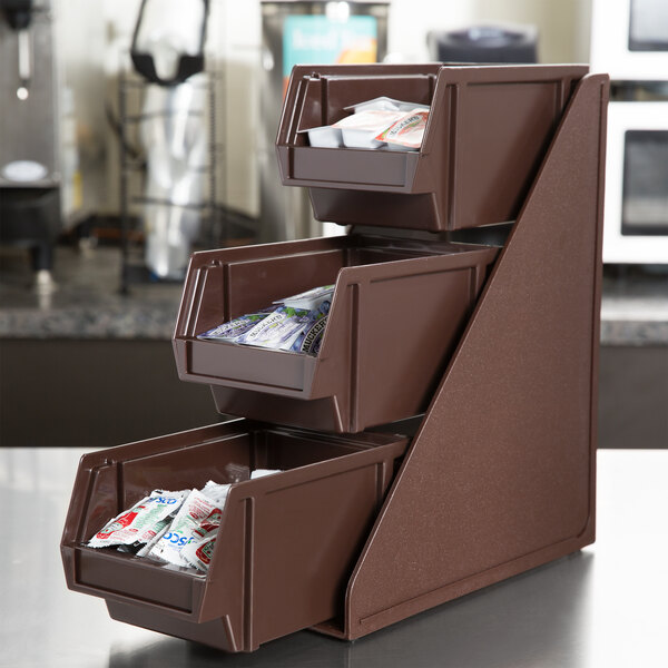 A brown plastic three-tier stand with brown plastic bins filled with small packets.