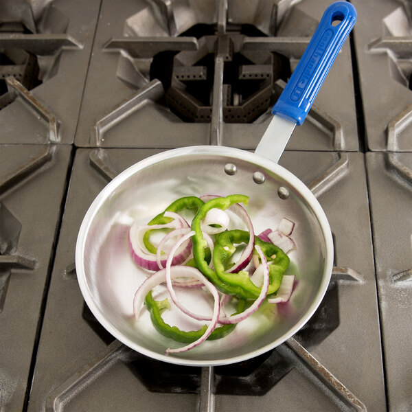A Vollrath Wear-Ever aluminum fry pan with sliced peppers and onions cooking on a stove.
