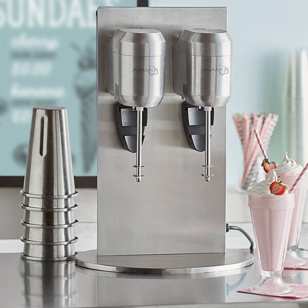 A white AvaMix freestanding milkshake machine with two cups of pink milkshakes with strawberries on the table.