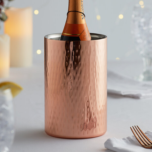 A bottle of champagne in a copper cylinder wine cooler.