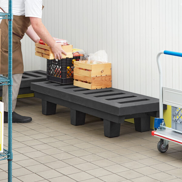 A man using a Regency black plastic dunnage rack to hold crates.