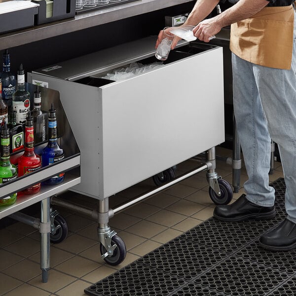 A person putting ice into a Regency stainless steel ice bin with a sliding lid.