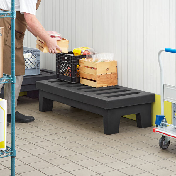 A man using a black plastic Regency Dunnage Rack to carry crates in a warehouse.