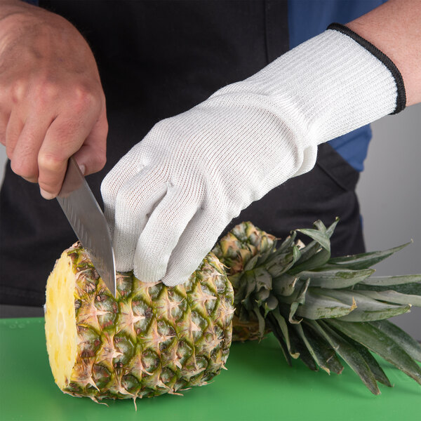 A person using a San Jamar D-Shield cut-resistant glove to cut a pineapple with a knife.
