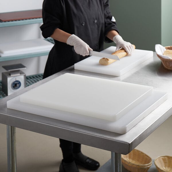 A person cutting bread on a Thunder Group white polyethylene cutting board system.