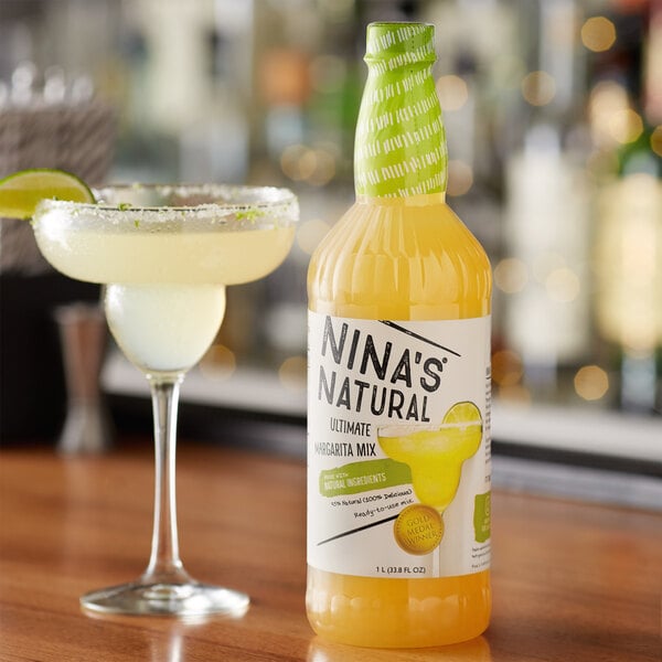 A bottle of Nina's Natural Ultimate Margarita Mix next to a glass of margarita with lime.