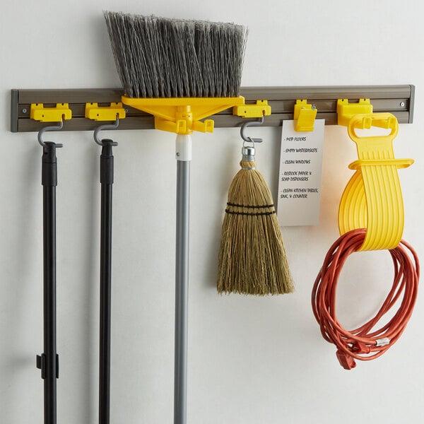 A Rubbermaid closet organizer holding brooms and mops on a wall.