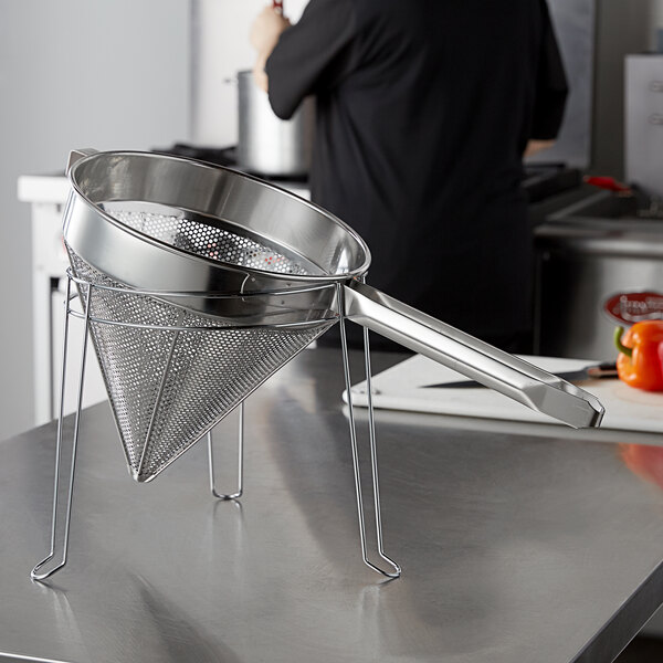 A stainless steel China cap strainer in a metal stand.