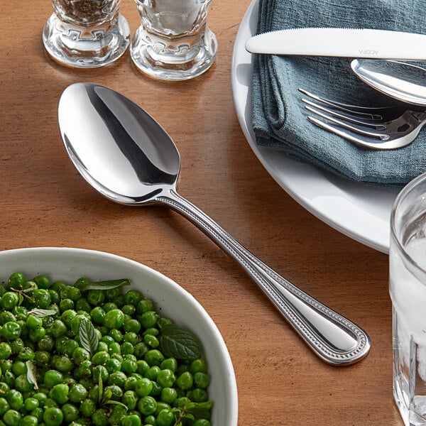 An Acopa stainless steel serving spoon in a bowl of peas on a white plate.