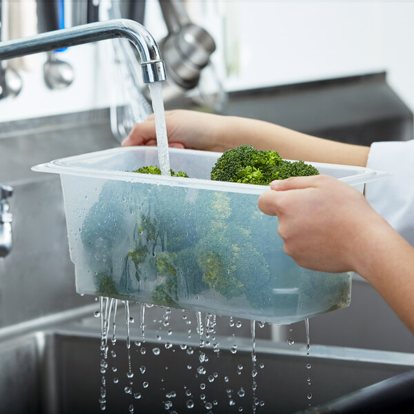 A person using a Cambro translucent polypropylene food pan colander to wash broccoli.