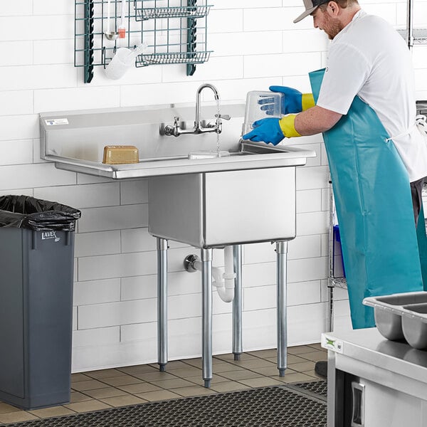 A man in a blue uniform and gloves washing a Steelton one compartment sink with a faucet over a left drainboard.