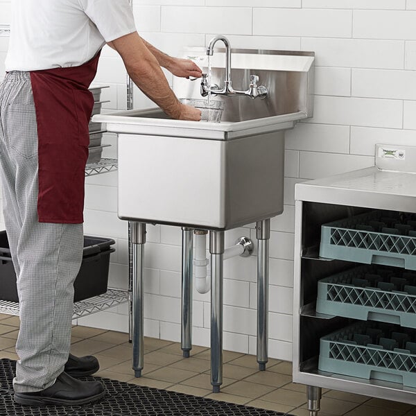 A man in a red apron washing his hands in a Regency stainless steel commercial sink.