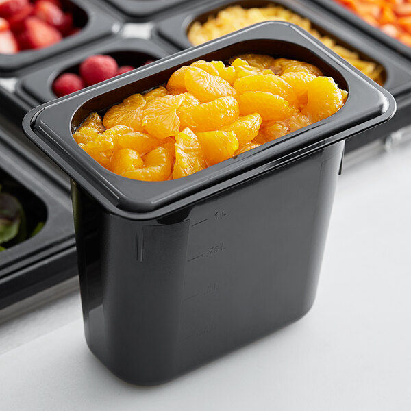 A black Cambro 1/9 size food pan filled with oranges on a table in a salad bar.