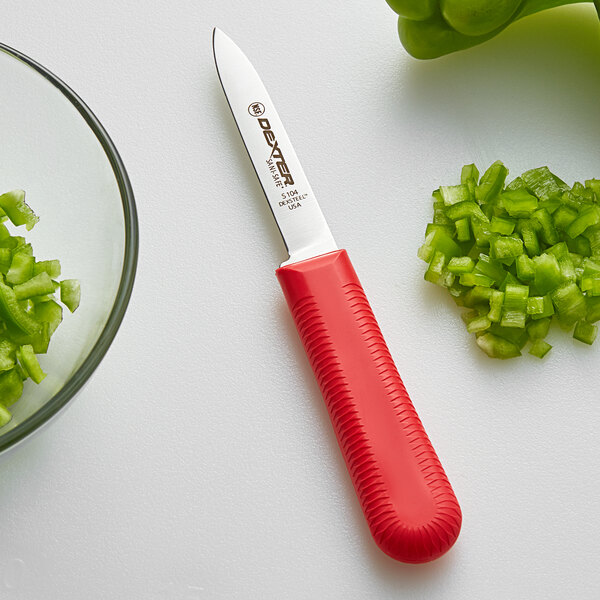 A Dexter-Russell Sani-Safe Cook's Style Paring Knife with a red handle next to a pile of chopped green peppers.