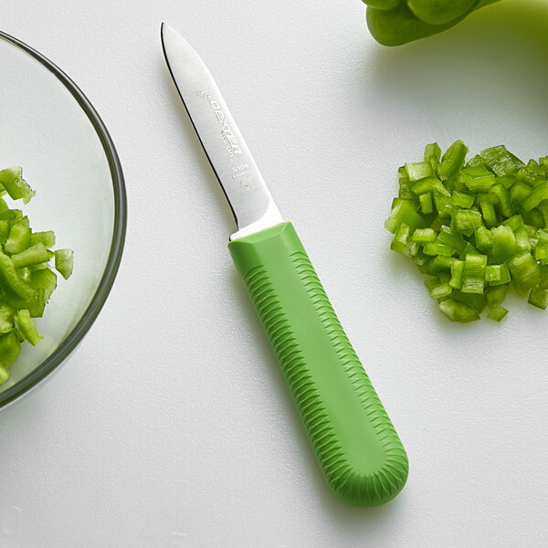 A Dexter-Russell green paring knife next to a bowl of chopped green peppers.