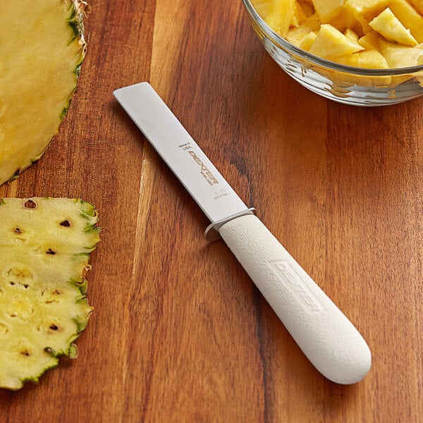 A Dexter-Russell Sani-Safe produce knife next to a bowl of pineapple chunks.