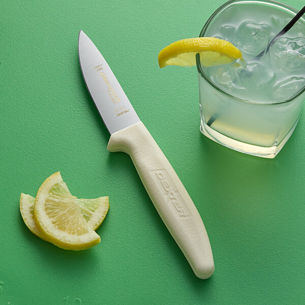 A Dexter-Russell utility knife next to lemon slices on a green surface.