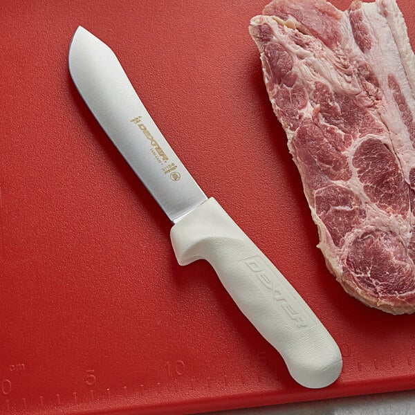 A Dexter-Russell Sani-Safe butcher knife next to a piece of meat on a cutting board.