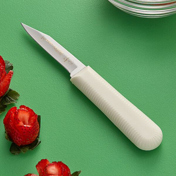 A Dexter-Russell Sani-Safe paring knife with a green handle cutting strawberries on a green surface.