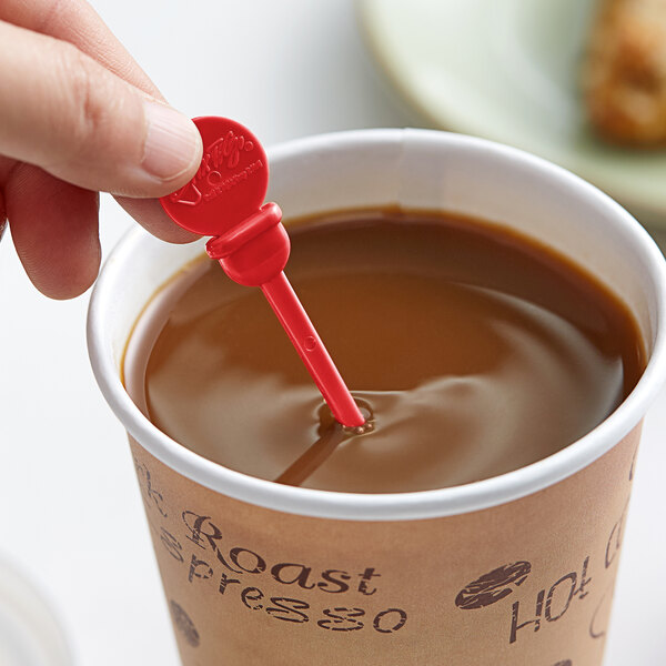 A hand holding a Royal Paper red plastic beverage stirrer in a cup of coffee.