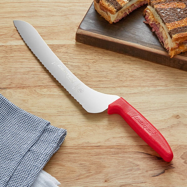 A Dexter-Russell bread knife with a red handle cutting a sandwich.