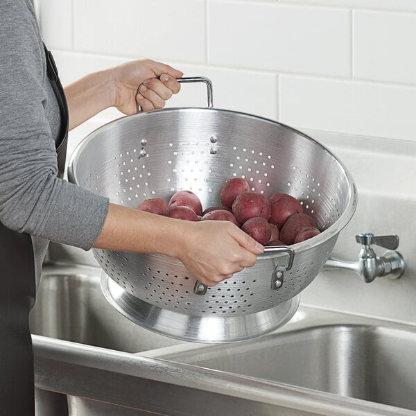 A woman using a Carlisle aluminum colander to strain red potatoes over a sink.