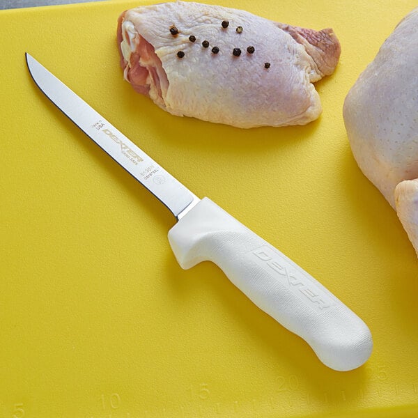 A Dexter-Russell narrow boning knife on a cutting board with a raw chicken breast.