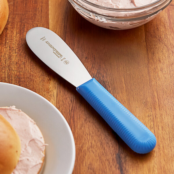 A Dexter-Russell blue smooth sandwich spreader with bread and butter on a plate.