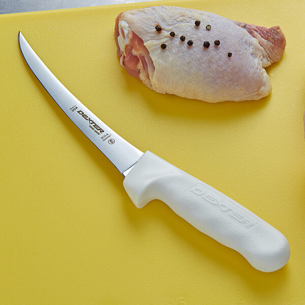A Dexter-Russell narrow curved boning knife next to a raw chicken breast on a cutting board.