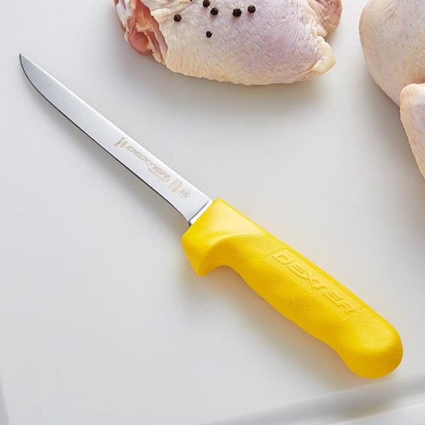 A Dexter-Russell narrow boning knife with a yellow handle on a cutting board with a chicken.