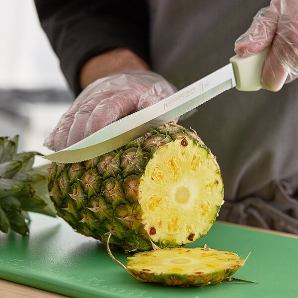 A person using a Dexter-Russell Sani-Safe scalloped utility slicer to cut a pineapple.