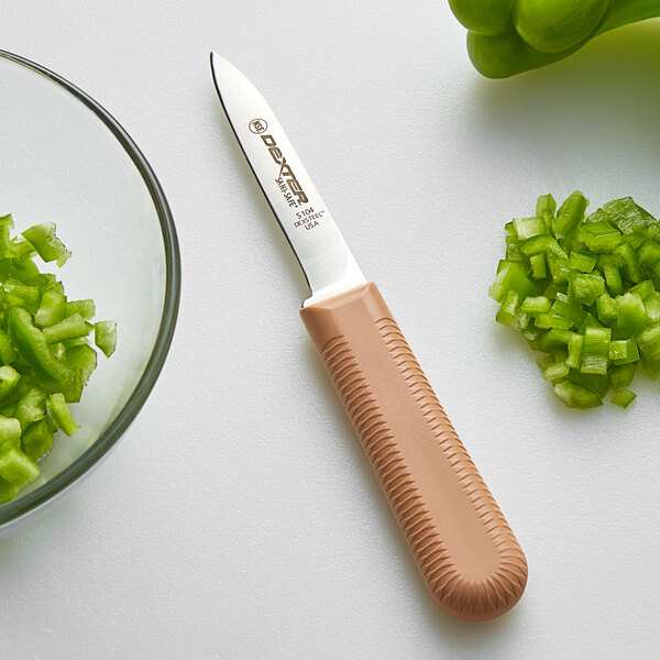A Dexter-Russell Sani-Safe paring knife with a brown handle next to a bowl of chopped green peppers.
