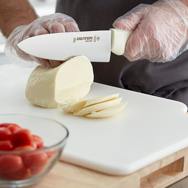 A person using a Dexter-Russell Sani-Safe chef knife to cut cheese on a cutting board.