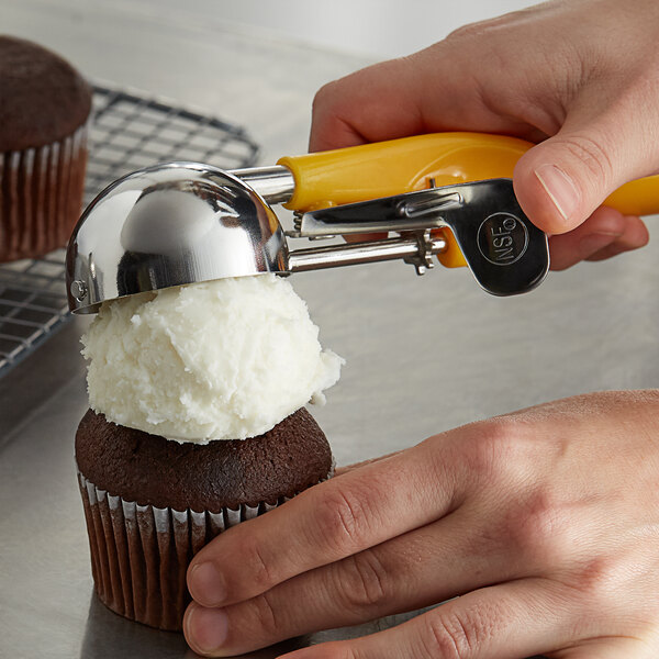 A person using a yellow Thunder Group ice cream scooper to scoop a cupcake.