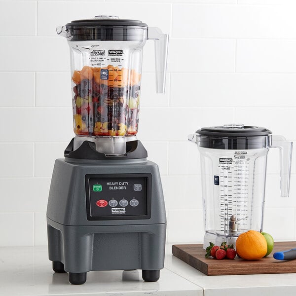 A Waring commercial food blender with fruit in it on a counter.