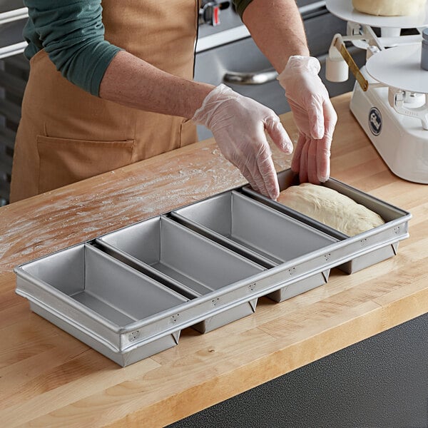 A person wearing gloves puts dough into a Baker's Mark aluminized steel bread loaf pan.