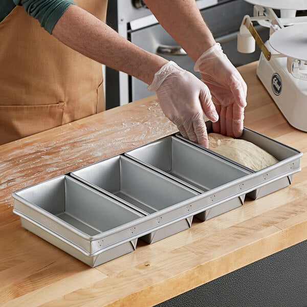 A person wearing gloves putting dough into a Baker's Mark aluminized steel bread loaf pan.