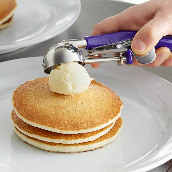 A person using a Thunder Group purple thumb press scooper to scoop butter on a stack of pancakes.